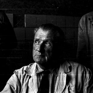 A solemn, weathered man in dim lighting.