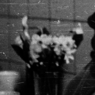 Nurse in cap sitting by bed with flowers.