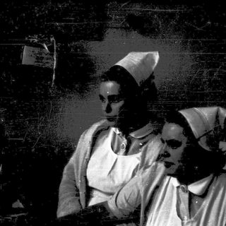 Nurses in traditional caps attending to patient.