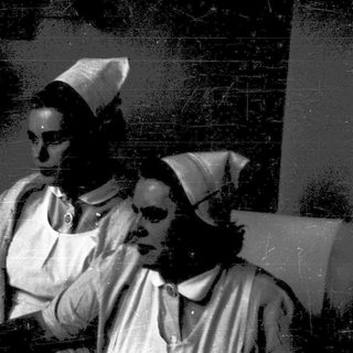 Nurses in traditional caps attending to patient.