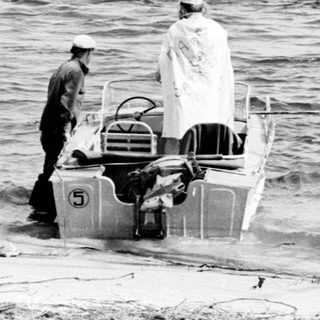 Two people launching small motorboat into water.