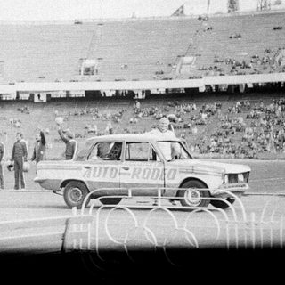 Classic car rally entering stadium with spectators.