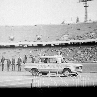 Classic car rally entering stadium with spectators.
