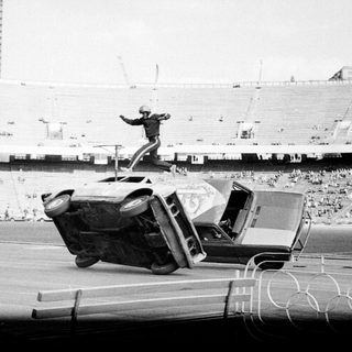 Stunt performer flips vintage car mid-air at stadium event.