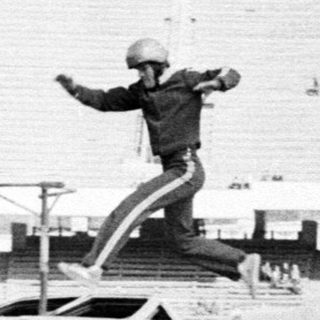 Stunt performer flips vintage car mid-air at stadium event.
