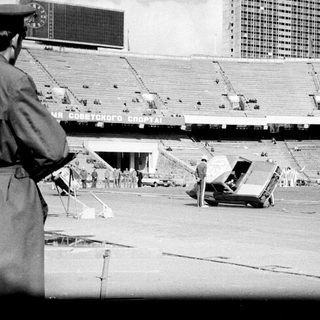 Empty stadium with construction vehicles, security personnel, and tents.