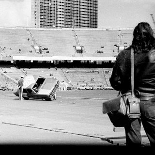Empty stadium with construction vehicles, security personnel, and tents.