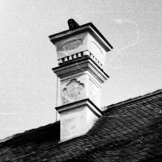 Black-and-white photo of a chimney on a tiled roof.