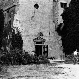 Abandoned building with crumbling facade, overgrown entrance, and two people.