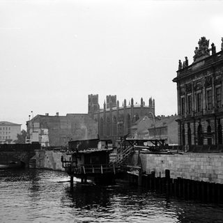 Historic black-and-white cityscape with riverfront buildings and bridge.