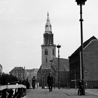 Black-and-white city street with historic church tower.
