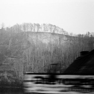 Blurred train view of misty, forested hillside.