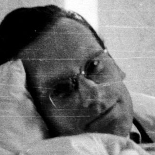 A person lying in bed wearing glasses.