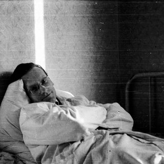 A person lying in bed wearing glasses.