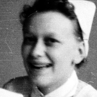 Nurses in traditional white uniforms smiling indoors.
