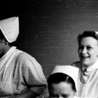 Nurses in traditional white uniforms smiling indoors.