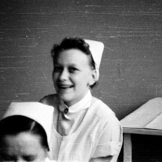 Nurses in traditional white uniforms smiling indoors.