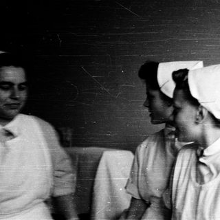Nurses in traditional white uniforms and caps.