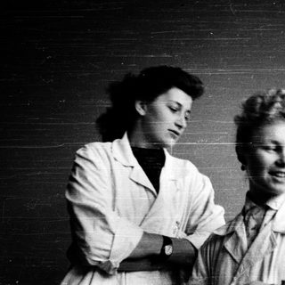 Two women in lab coats posing together, mid-20th century.