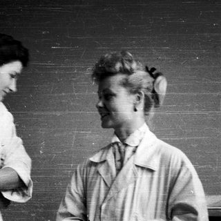 Two women in lab coats conversing indoors.