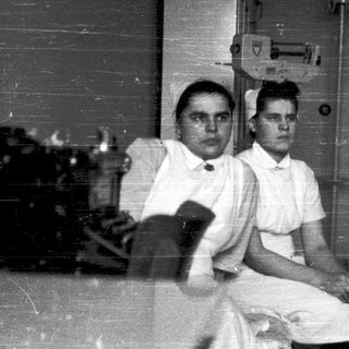 Nurses posing indoors with vintage medical equipment.