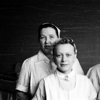 Three nurses in vintage uniforms posing indoors.