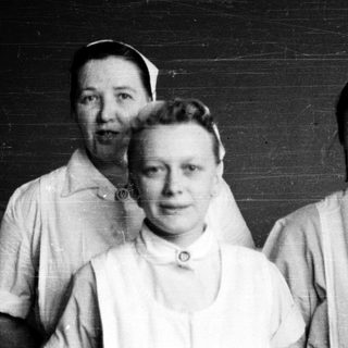 Three nurses in vintage uniforms posing indoors.