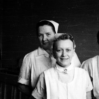 Three nurses in vintage uniforms posing together.