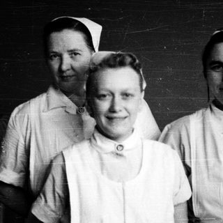 Three nurses in vintage uniforms posing together.