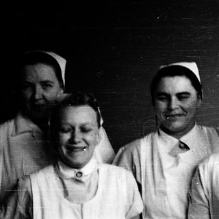 Four nurses in vintage uniforms posing together.