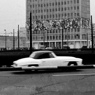 High-rise building with mural, vintage car, urban street scene.