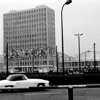High-rise building with mural, vintage car, urban street scene.