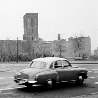 Vintage car passing old stone church building.