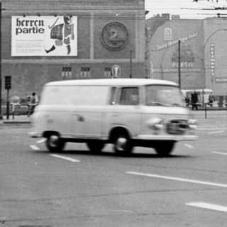 Vintage city street with vintage vehicles and billboards.