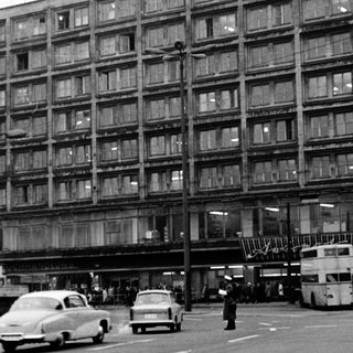 Large multi-story building with vintage cars and bus.