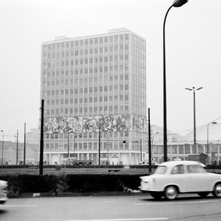 High-rise building with mural, vintage cars, urban street scene.