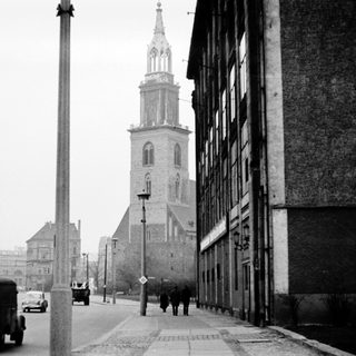 Black-and-white city street scene with vintage vehicles and historic church tower.