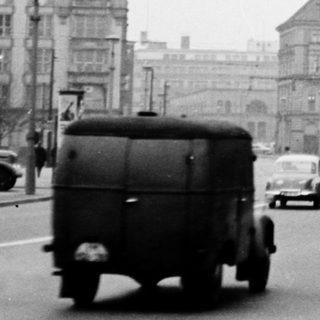 Black-and-white city street scene with vintage vehicles and historic church tower.