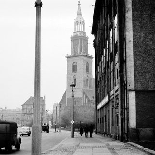 Black-and-white city street scene with vintage vehicles and historic church tower.