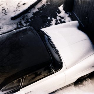 Classic car parked in snowy, dirty alley.