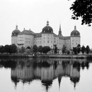 Grand historic castle reflected in calm lake.