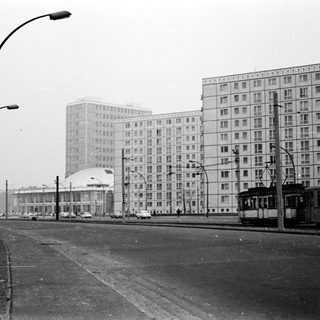 Urban street scene with high-rise apartment blocks, tram, and 1960s-era architecture.