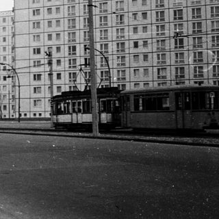 Urban street scene with high-rise apartment blocks, tram, and 1960s-era architecture.