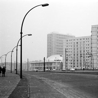 Urban street scene with high-rise apartment blocks, tram, and 1960s-era architecture.