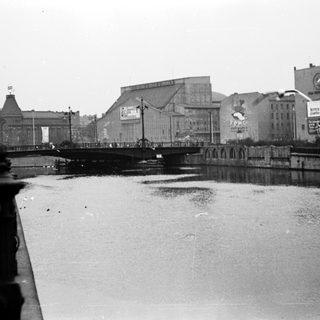 Black-and-white cityscape with bridge over river.