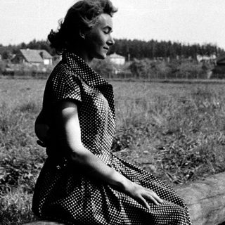 Woman sitting on log in rural field.