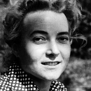 Young woman in patterned blouse outdoors, smiling.