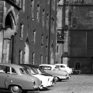 Historic European building with classic architecture, vintage cars parked.