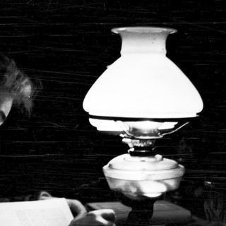Person reading letter by kerosene lamp.