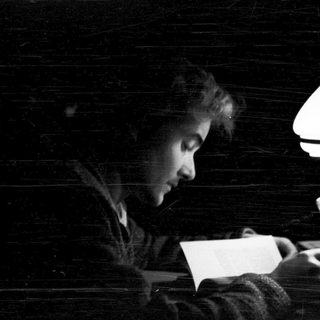 Person reading letter by kerosene lamp.